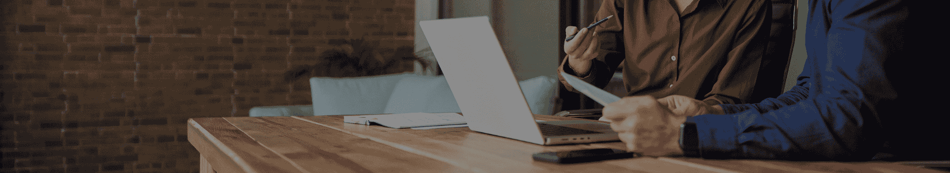 Bureau avec un ordinateur des documents et téléphone avec au dessus les mains d'une femme tenant un stylo et les mains d'un homme tenant une feuille