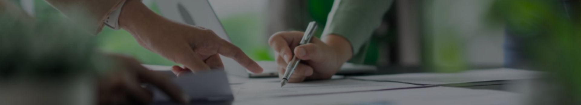 La main d'un homme pointe des feuilles sur un bureau et la main du femme écrit avec un stylo sur ces feuilles