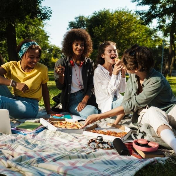 Groupe de 4 étudiants qui rigolent autour d'un pique-nique dans un parc