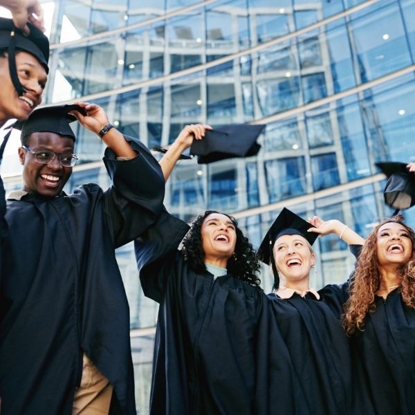 Etudiants en toge jetant leur chapeau à leur remise de diplôme avec des bâtiments en fond