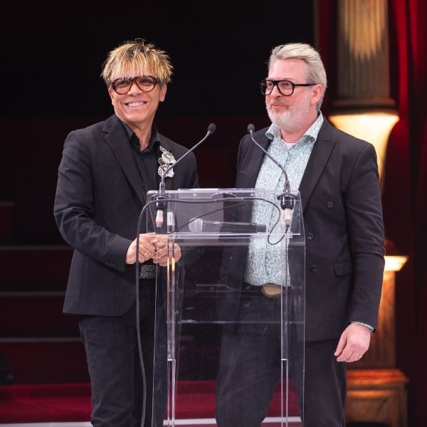 Nabil HAYARI, parrain de promotion, et son collaborateur Deux hommes en tenue professionnelle derrière un pupitre dans une salle de spectacle