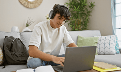Quand commencer à réfléchir à sa poursuite d'études post-bac ? Jeune homme avec un t-shirt blanc et un casque audio travaille sur un ordinateur portable dans son salon