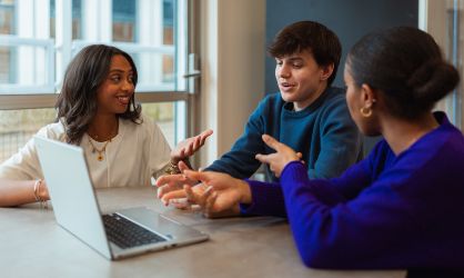 Trois étudiants travaillent devant un ordinateur portable et parlent ensemble