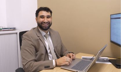 Homme en costume souriant et regardant face caméra assis à un bureau et cliquant sur un ordinateur portable 